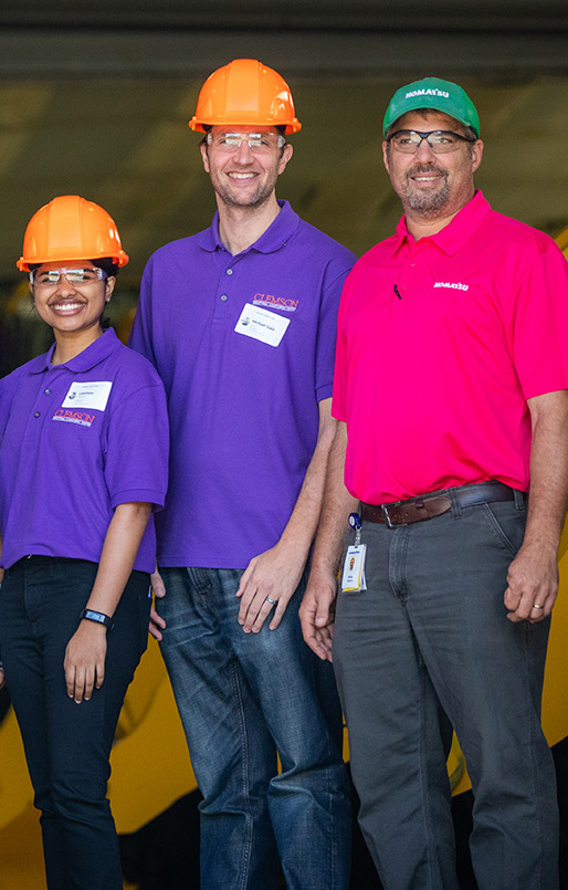 Two men and a woman smiling in hardhats.